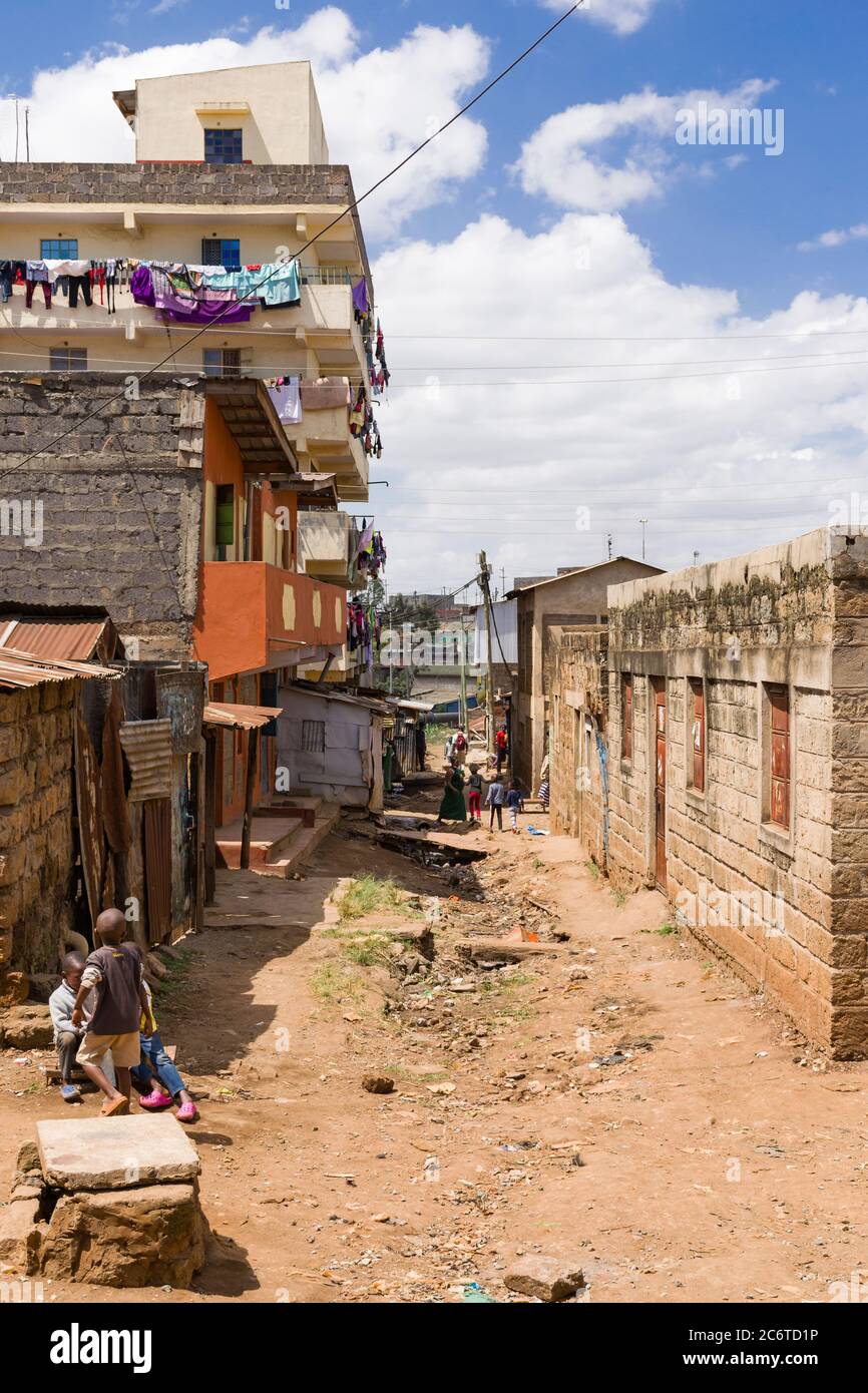 View down a dirt side alley with buildings, children and people in it, Korogocho slum, Kenya, East Africa Stock Photo
