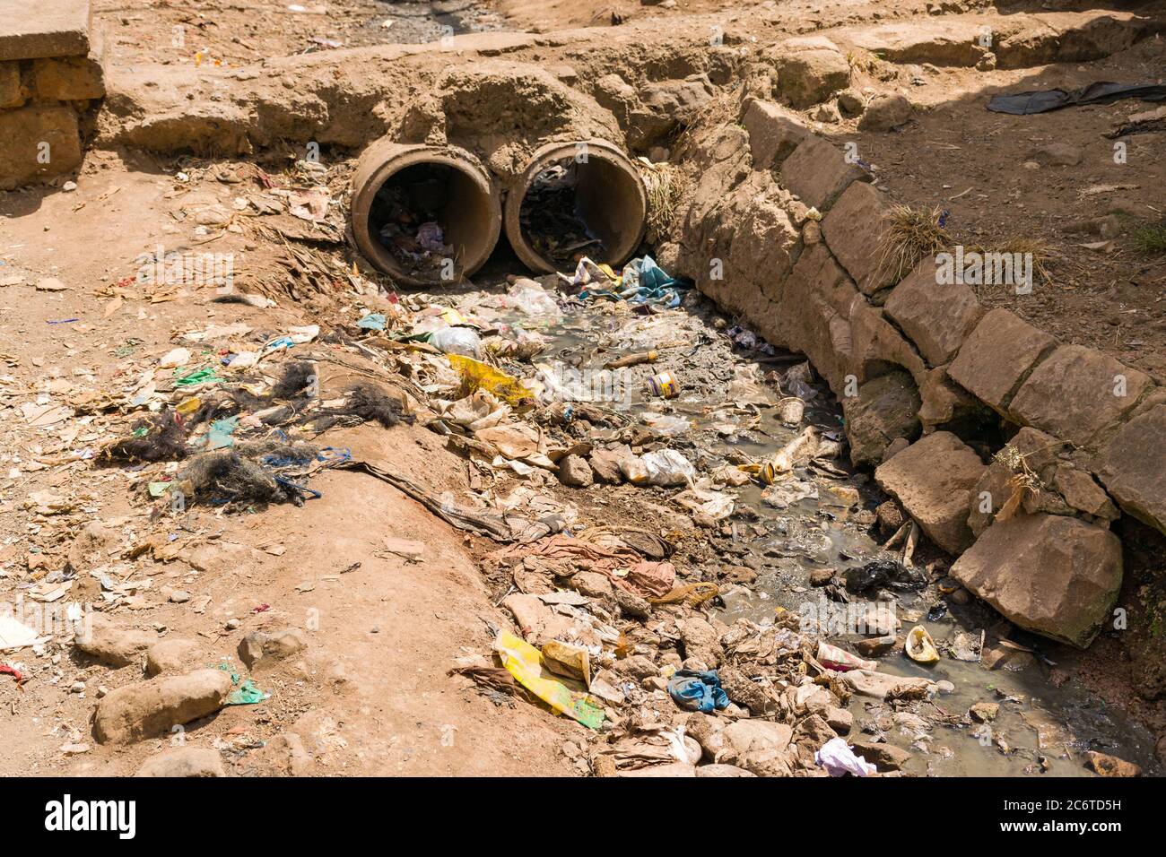 An open sewer filled with rubbish by the side of a dirt alley, Korogocho slum, Kenya, East Africa Stock Photo