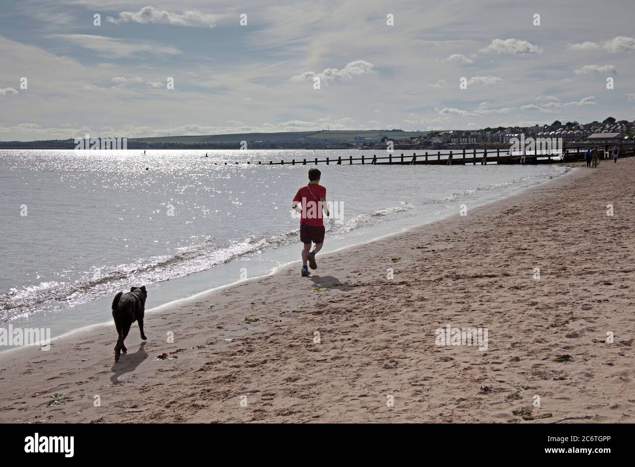 Portobello, Edinburgh, Scotland, UK 12 July 2020.Temperature 13 degrees in the morning rising to 18 degrees in afternoon with very little breeze. Pictured man running with his dog in pursuit very popular over the last three months of the Coronavirus pandemic as people of all ages have healthier pursuits in their leisure time. Stock Photo