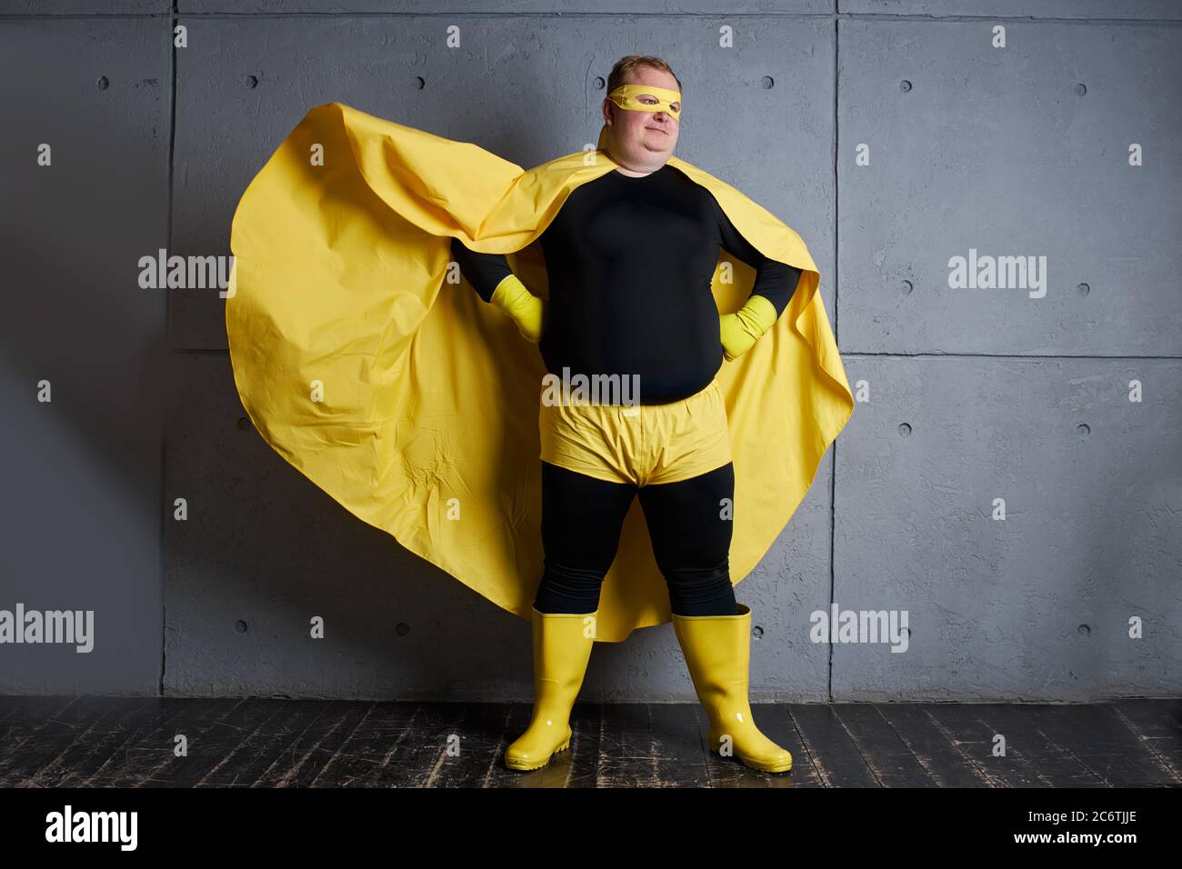 handsome brave strong man has a mad desire, a dream to shield the world from dirt and evil. fat superhero in yellow costume posing isolated over gray Stock Photo