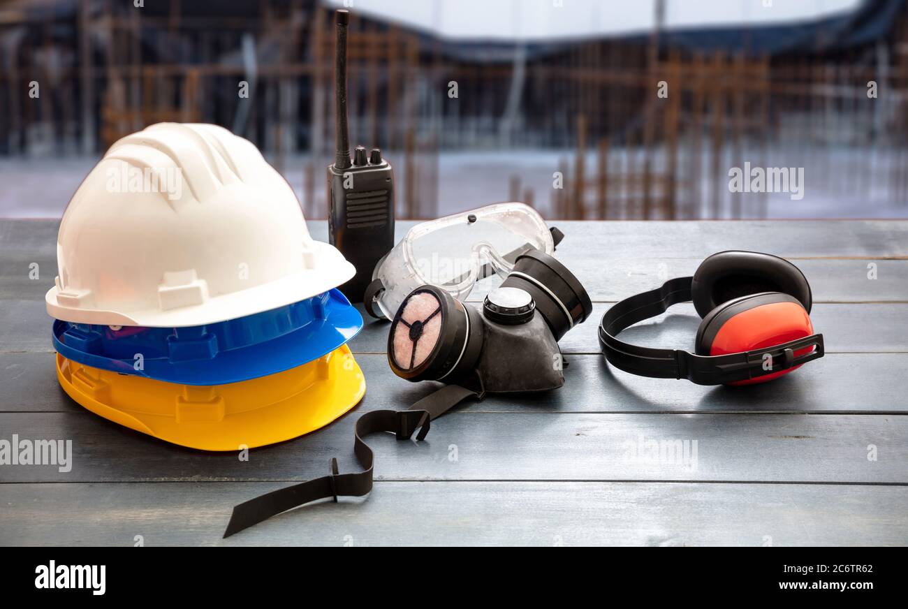 Work safety protection equipment. Industrial protective gear on wooden table, blur construction site background. Hardhats, earmuffs, respiratory mask, Stock Photo