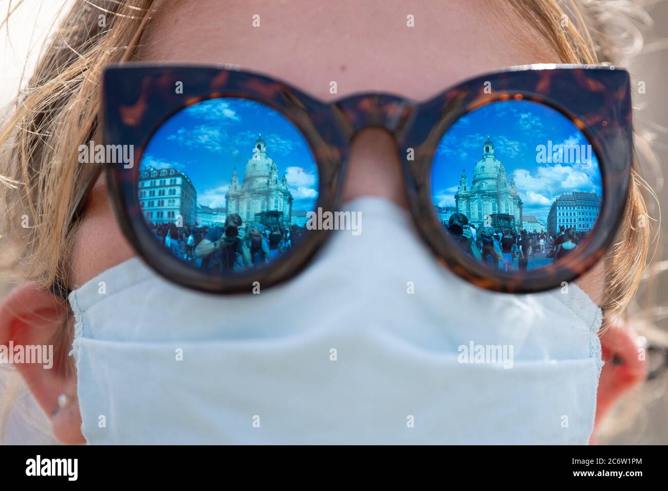 Dresden, Germany. 12th July, 2020. A participant in a demonstration against racism stands with a mouth guard on the Neumarkt while the Frauenkirche is reflected in her sunglasses. The rally of the 'Black Lives Matter Dresden' group wants to draw attention to structural racism after the violent death of George Floyd. Credit: Sebastian Kahnert/dpa-Zentralbild/dpa/Alamy Live News Stock Photo