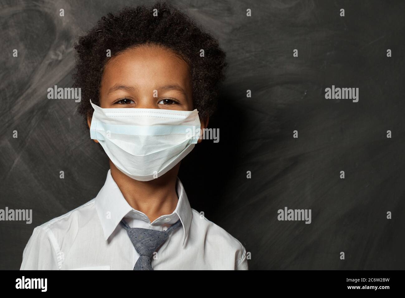 Black child boy in medical protective face mask on blackboard ...