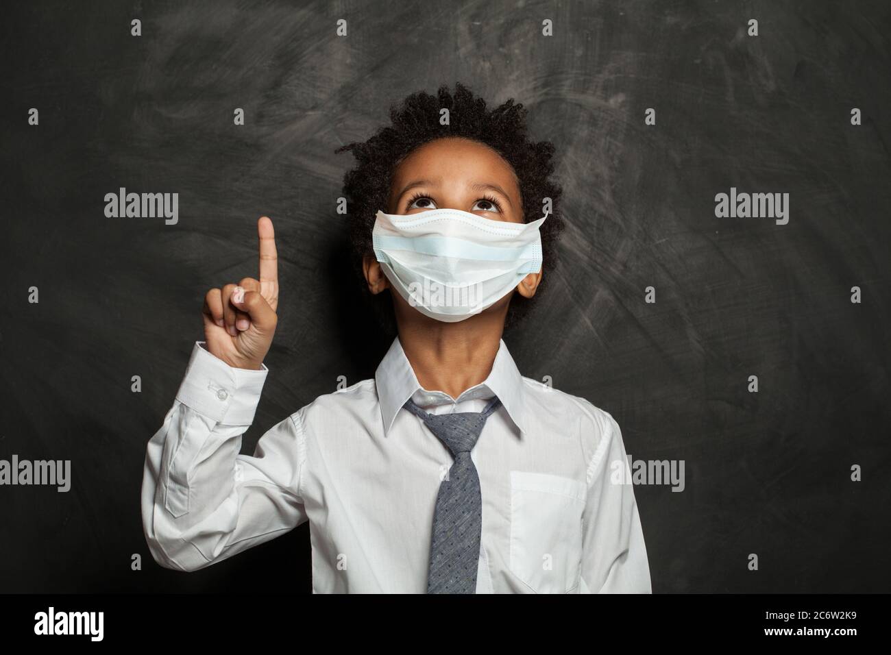 Black kid boy in medical protective face mask pointing up on blackboard ...
