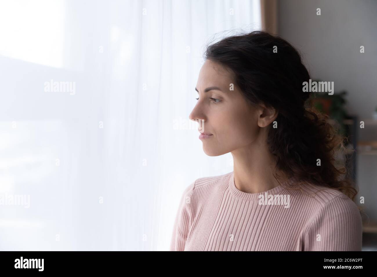 Pensive young woman look in window thinking or missing Stock Photo