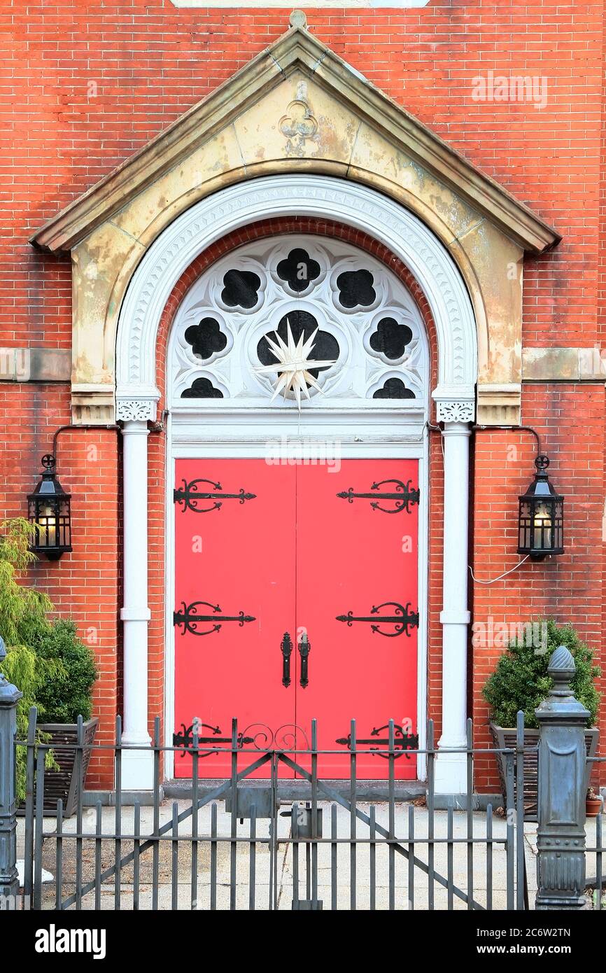 Red vintage arched wooden entry door with black handles and decorative hinges, white columns and molding, and limestone portal. New Jersey. USA. Stock Photo