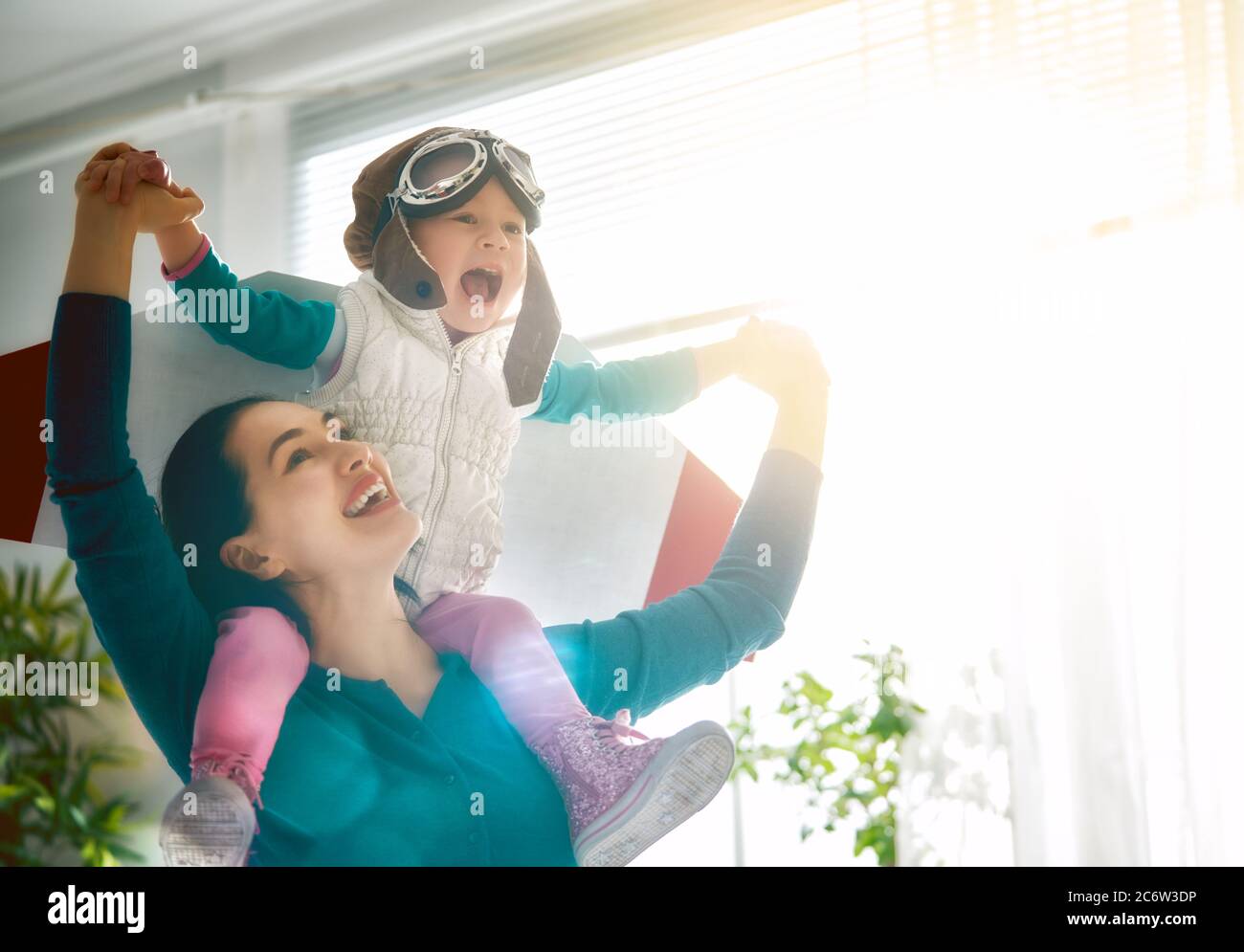 Happy family is having fun at home. Mother and her child girl playing together. Girl in pilot's costume. Stock Photo
