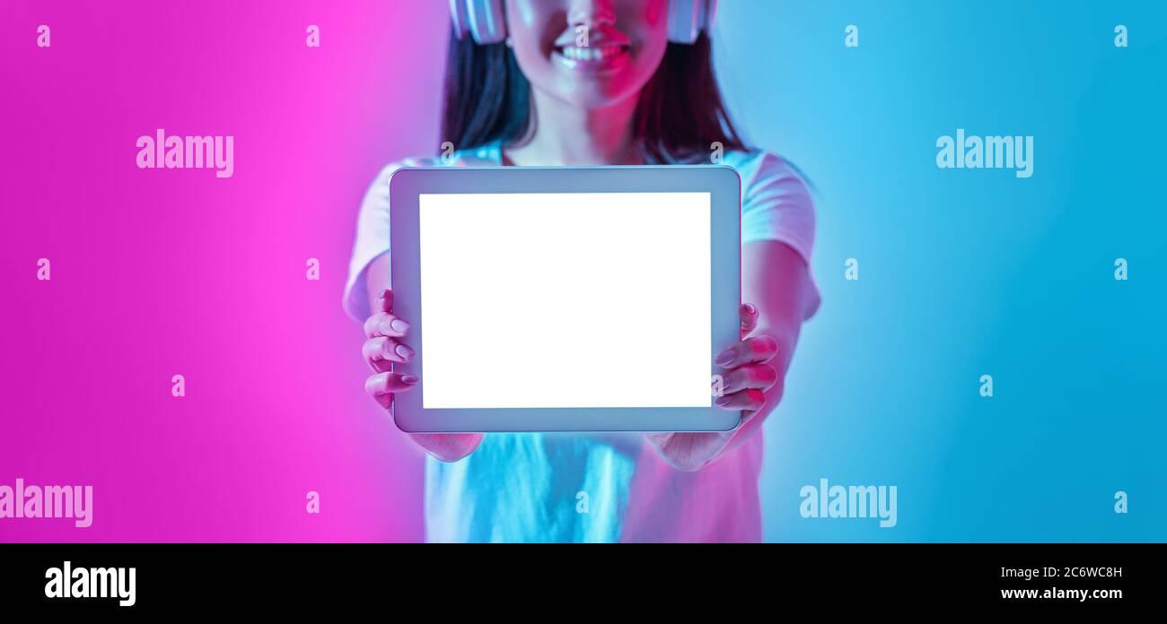 Rejoice to vin. Smiling girl in headphones shows tablet with blank screen Stock Photo