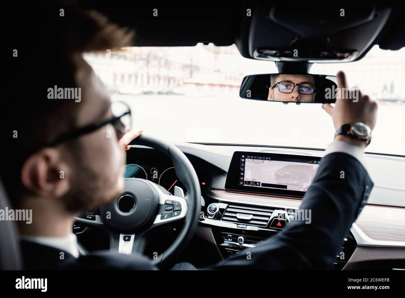 Young businessman driving alone adjusting rearview mirror Stock Photo