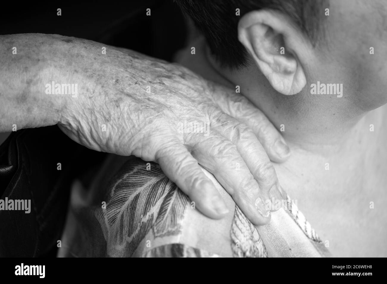 Close up of elderly man's hands gently massaging the shoulders of his wife in black and white Stock Photo