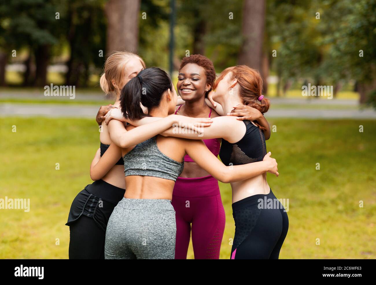 Diverse young girls in sportswear hugging after outdoor yoga class