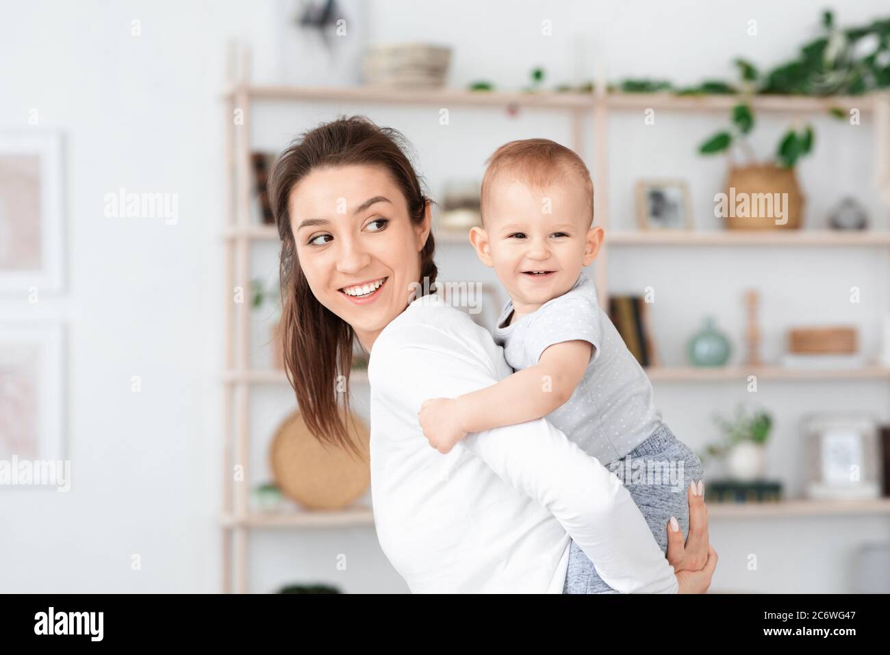 Happy Maternity. Mom Playing With Her Adorable Baby At Home, Piggybacking Him Stock Photo