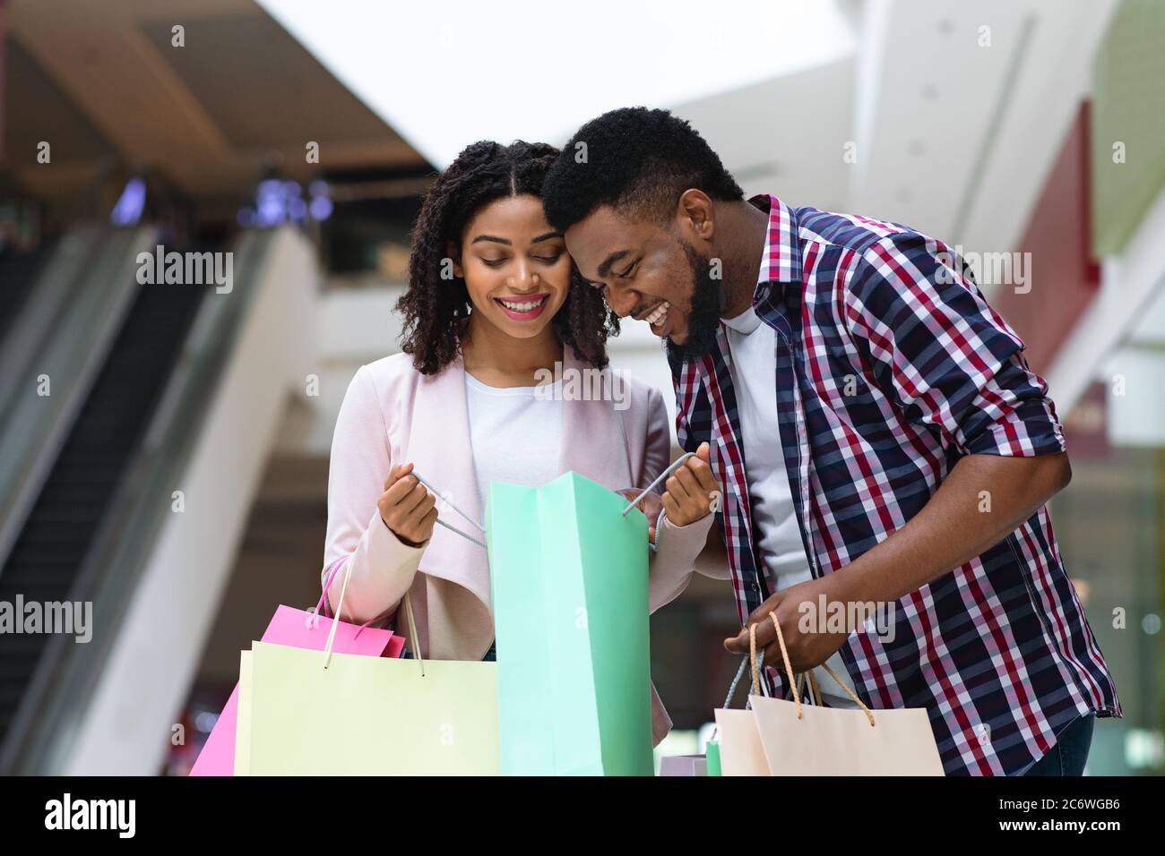 Happy black couple discussing purchases in shopping center, opening bags and smiling Stock Photo