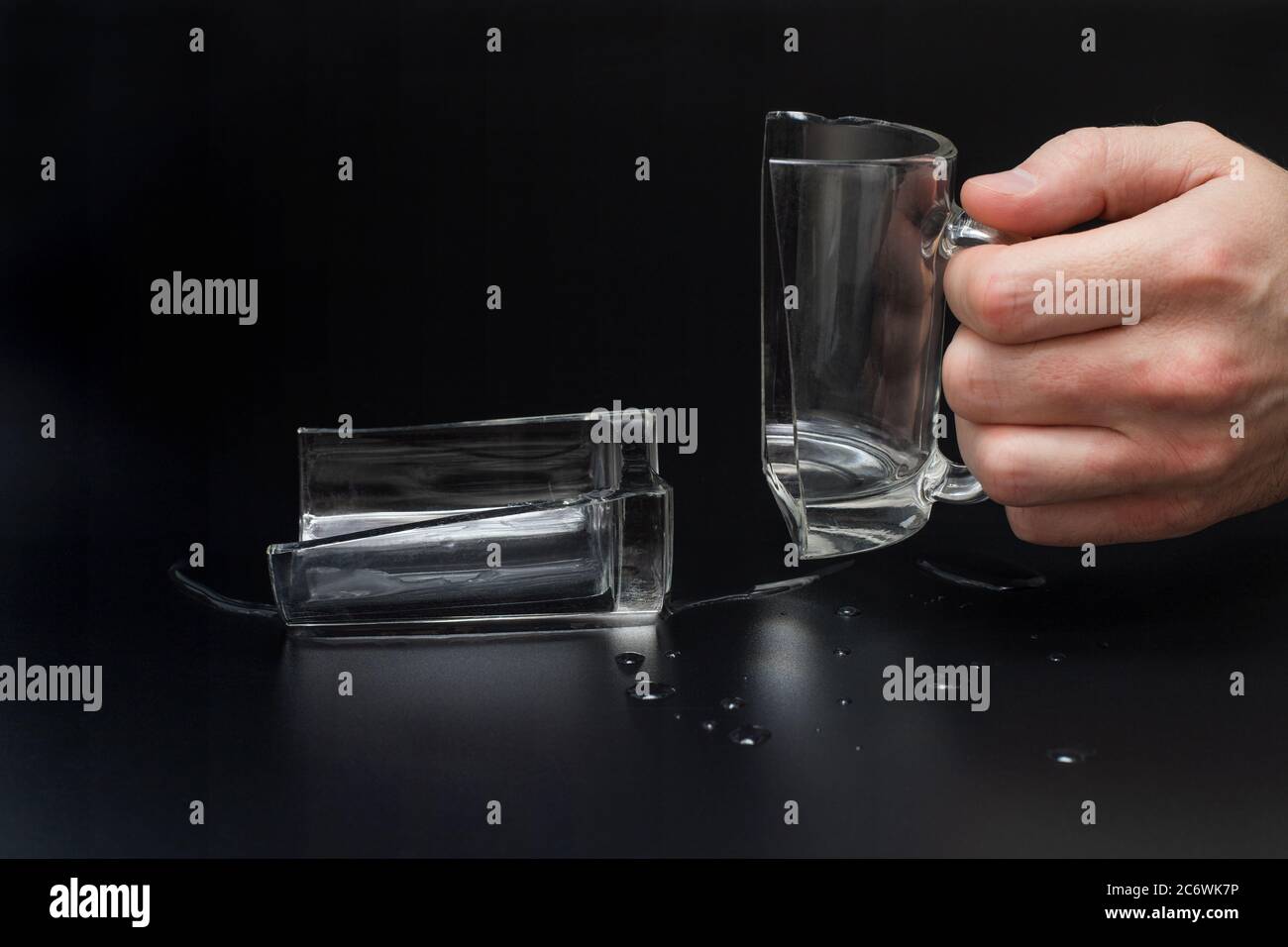 Man holds broken glass cup on black background, incident concept Stock