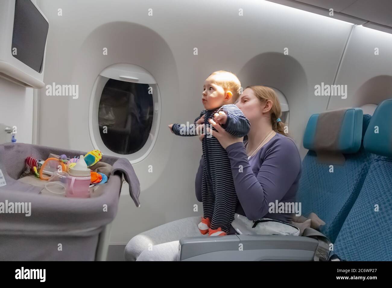 Infant plays on mother hands at the airplane. Amazed of tablet monitor and flight. baby bassinet on the foreground Stock Photo - Alamy