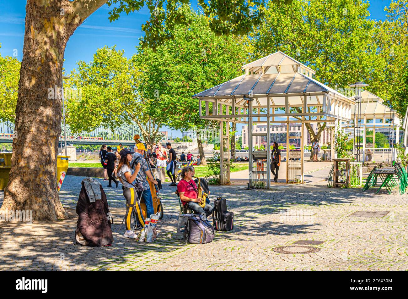 Cologne, Germany, August 23, 2019: street musicians are playing their instruments under green trees in historical city centre, blue sky background Stock Photo