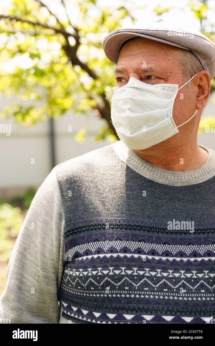 Portrait of mature man in medical mask in garden. Close up of older male protecting yourself from diseases in period coronavirus epidemic infection. Stock Photo