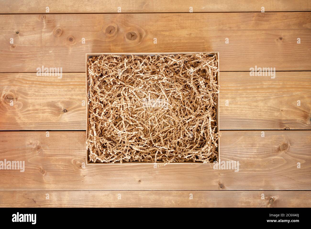 Opened gift box with shredded paper on wooden background. Flat lay, top