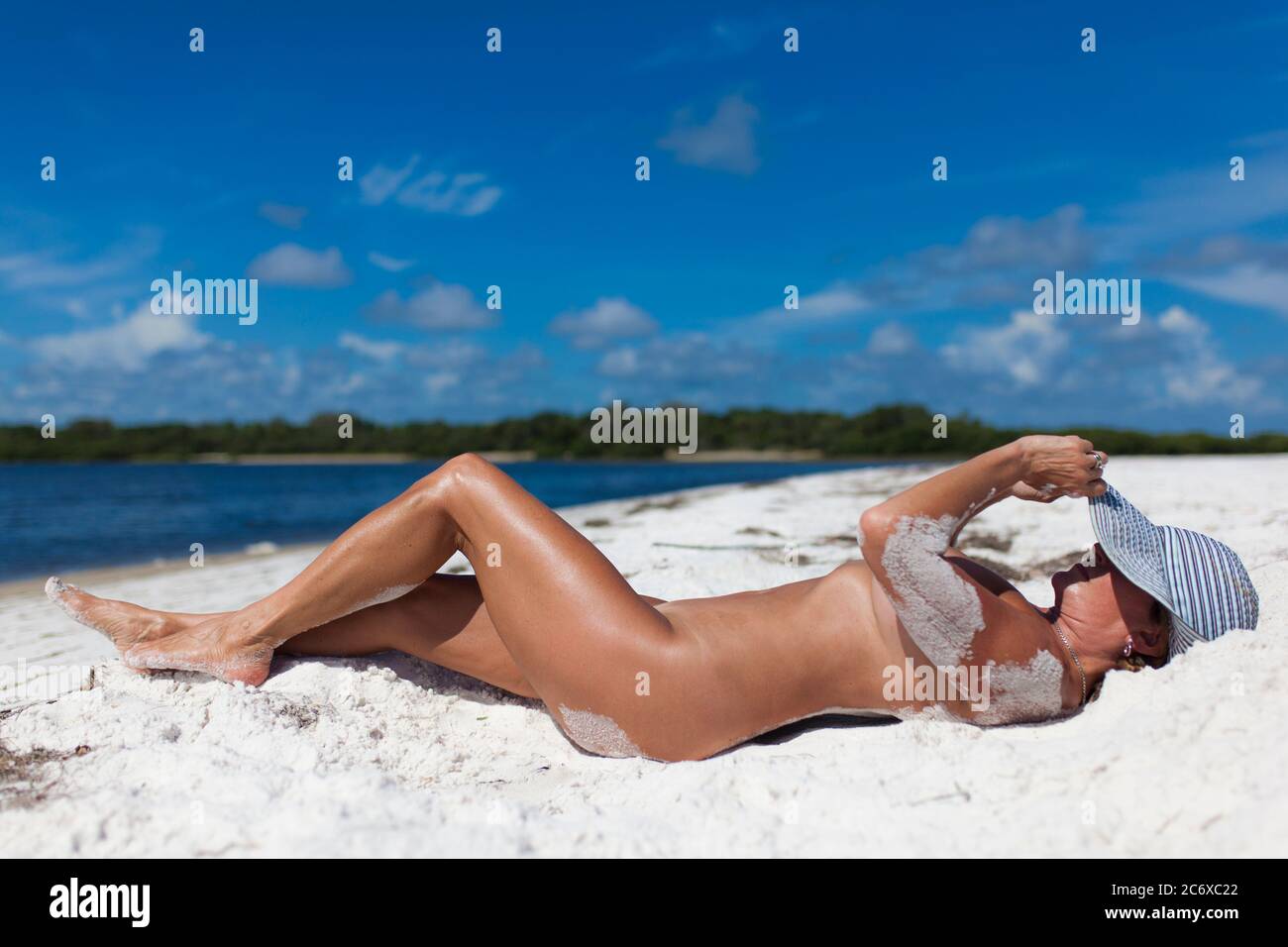 Naked woman sunbathing on a white sand beach Stock Photo