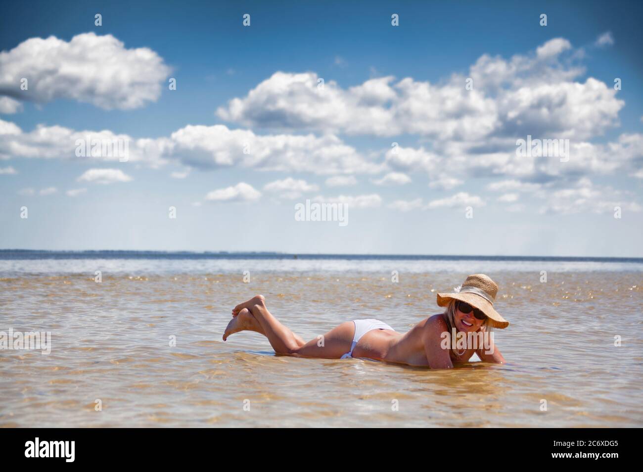 Topless woman lying on her stomach in the water with a big sunhat on Stock Photo