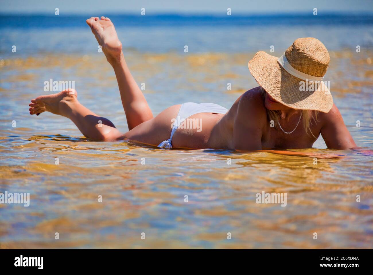 Topless woman lying on her stomach in the water with a big sunhat on Stock Photo