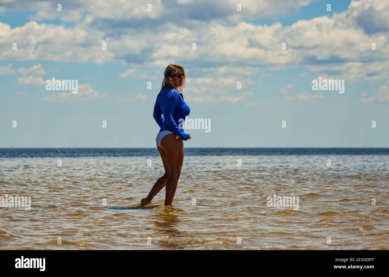 Physically Fit woman in a bikini with a blue cover up standing along the shoreline Stock Photo