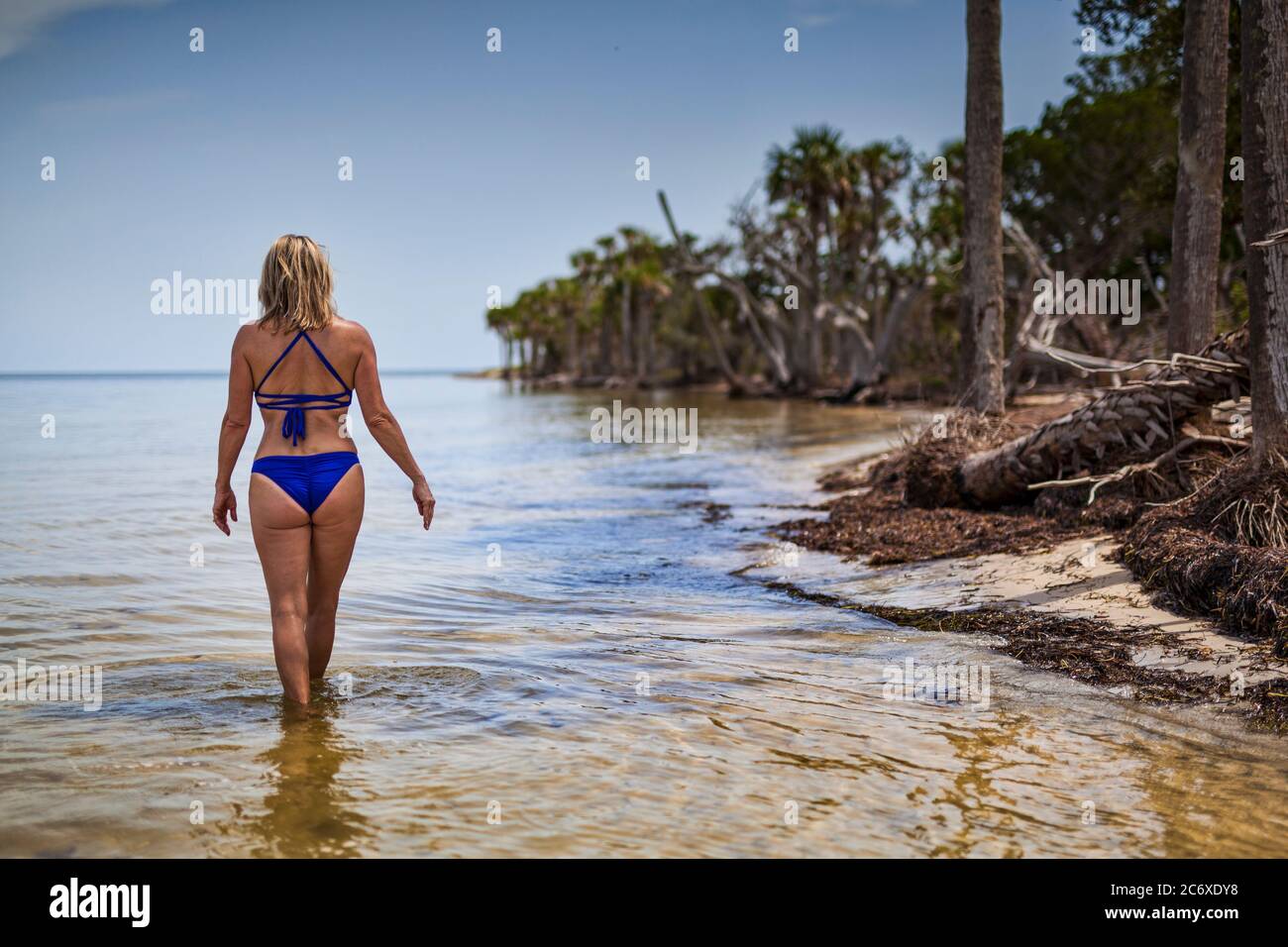 Woman in a blue two piece bikini walking along the shoreline Stock Photo