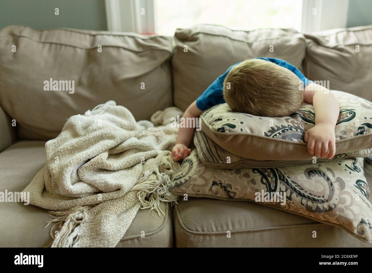 Tired young child asleep at home on couch lying on stacked pillows Stock Photo