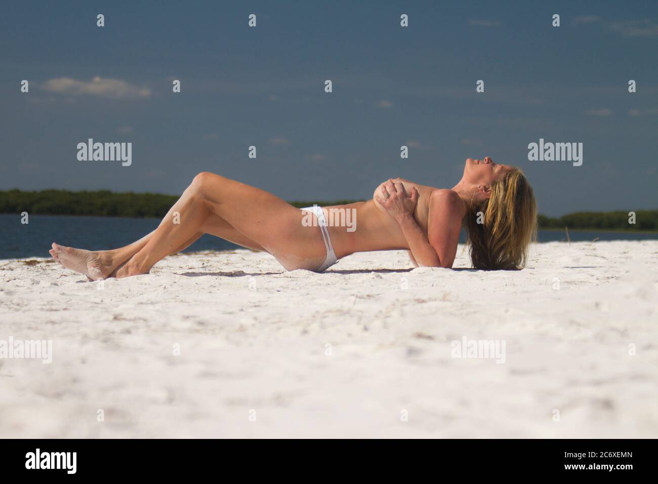 Physically fit blonde woman lying topless on a white sand beach Stock Photo
