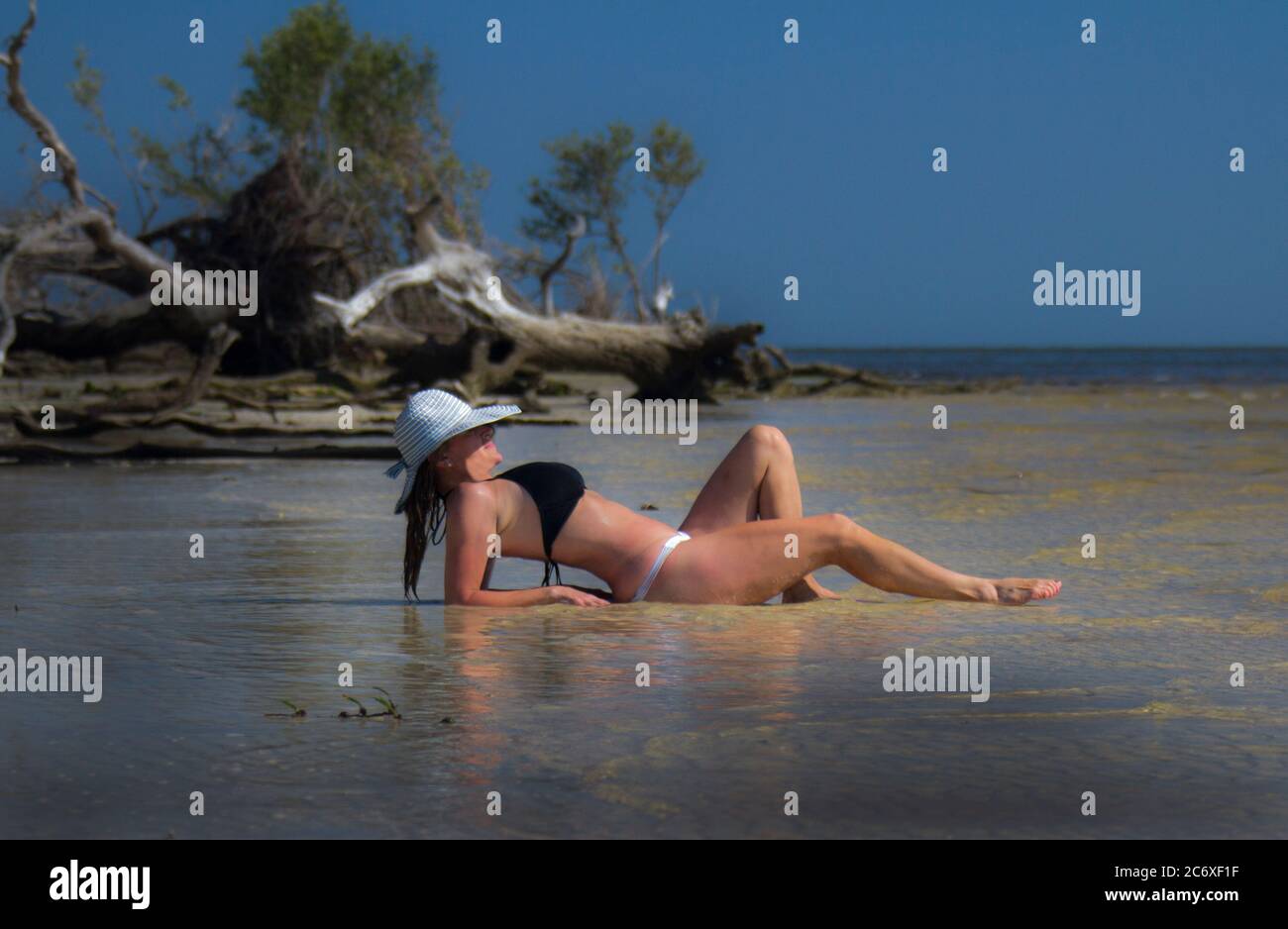 Bikini Clad woman lying on the shoreline of a white sand beach in a two piece bathing suit Stock Photo