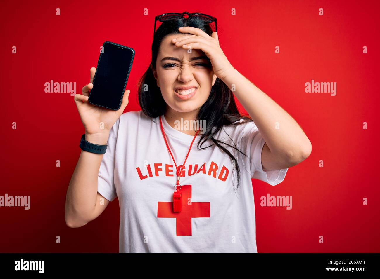 Young lifeguard woman showing smartphone screen over red background ...