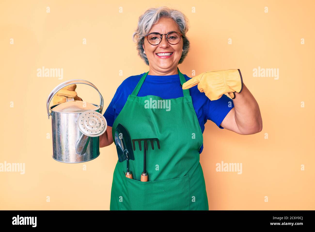 Senior hispanic grey- haired woman wearing gardener apron and gloves ...