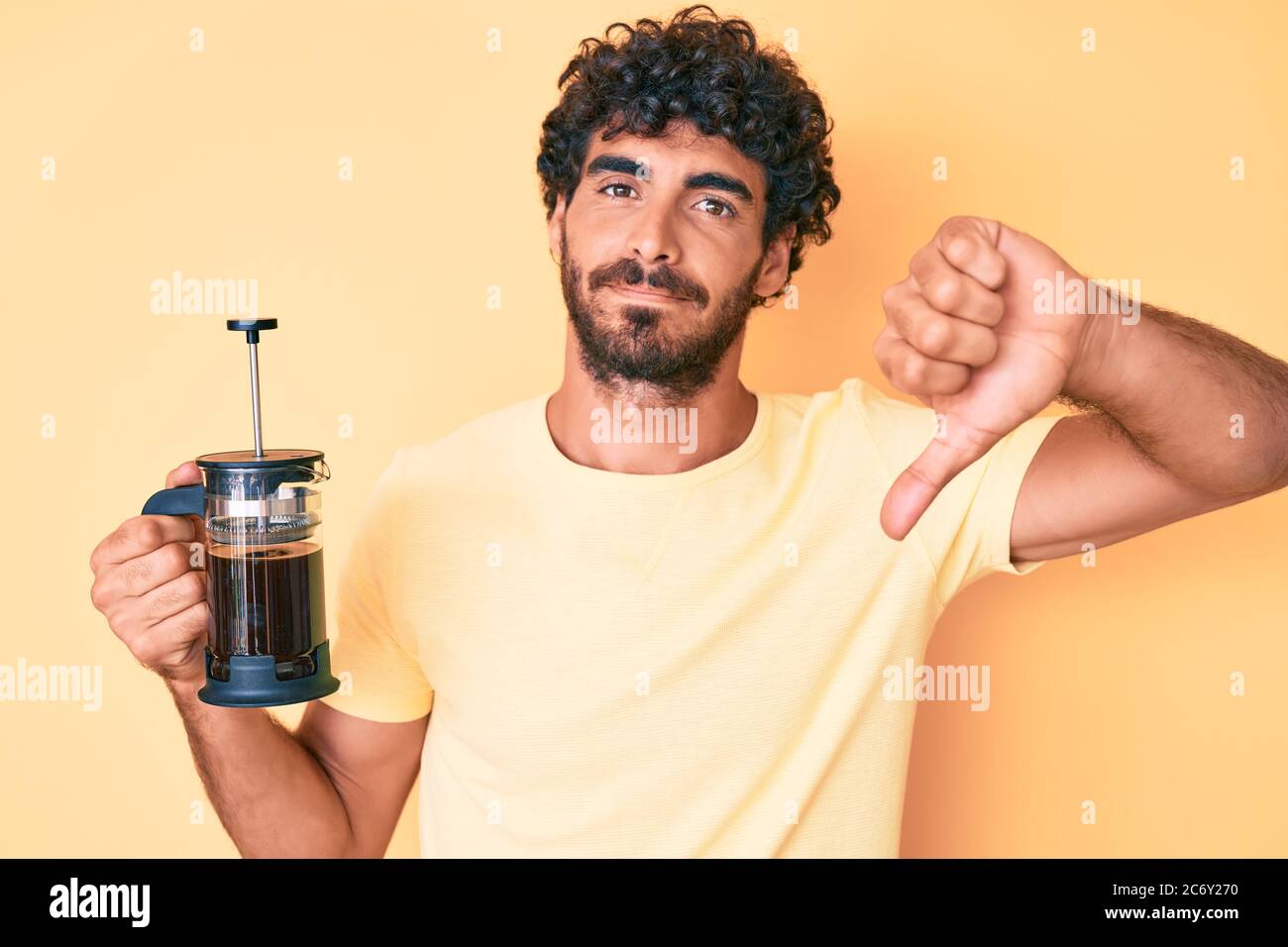 Handsome young man with curly hair and bear holding french coffee maker ...