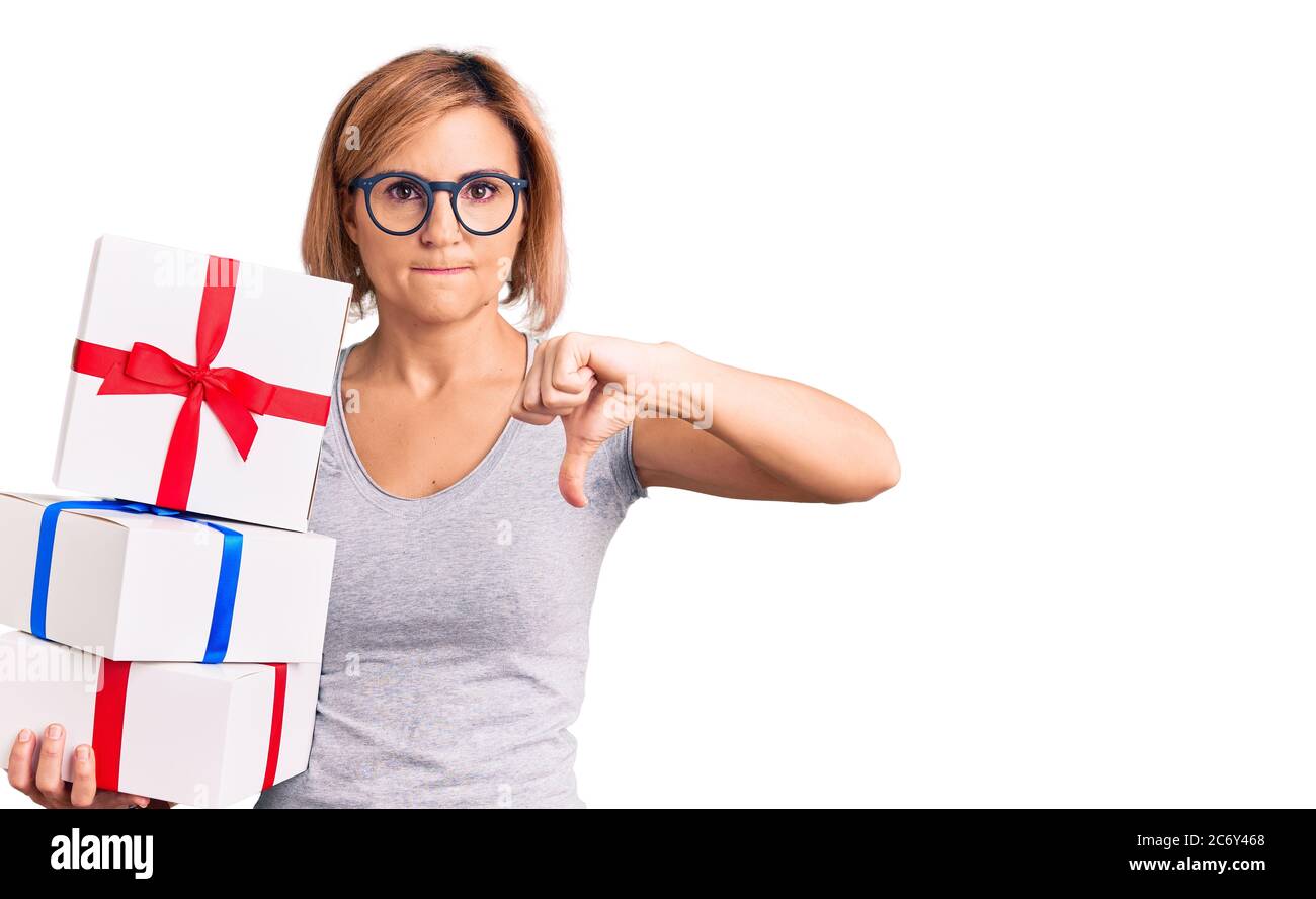 Young blonde woman wearing glasses holding gift with angry face, negative sign showing dislike with thumbs down, rejection concept Stock Photo