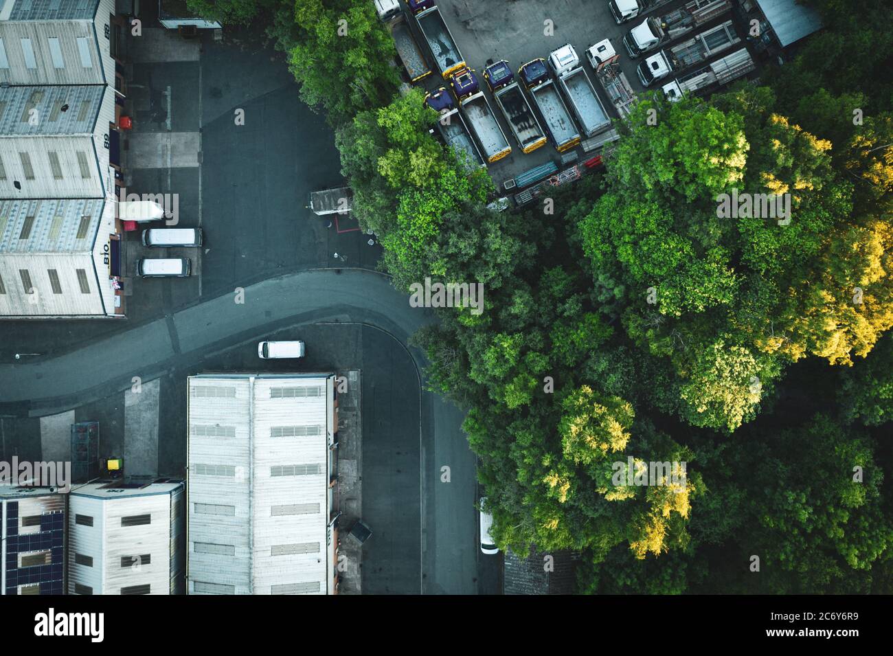 Top down aerial view over industrial buildings among green tree branches in United Kingdom Stock Photo
