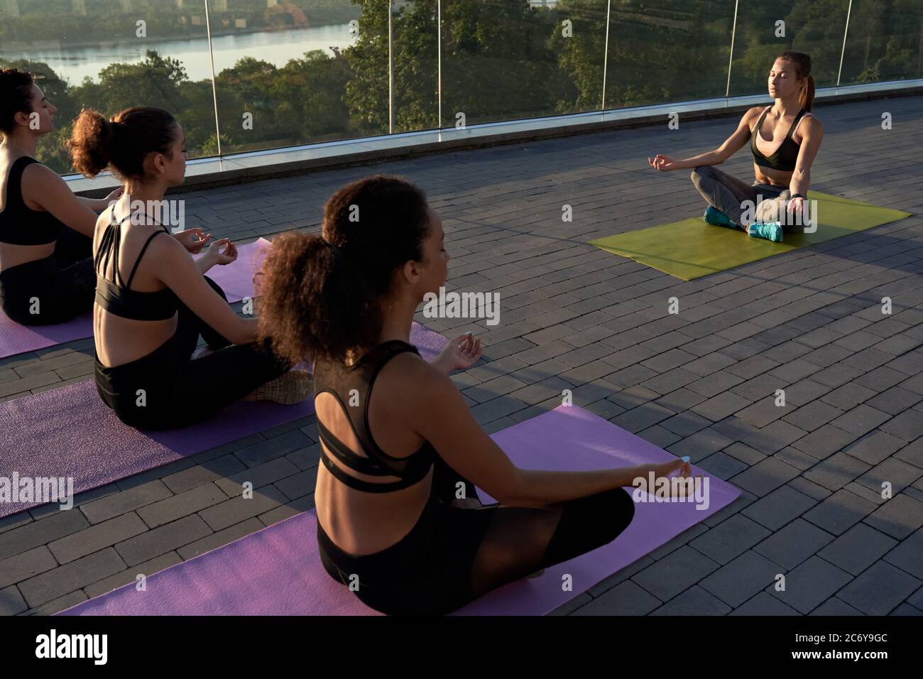 Multiethnic young women meditate with yoga teacher during group class outdoor. Stock Photo