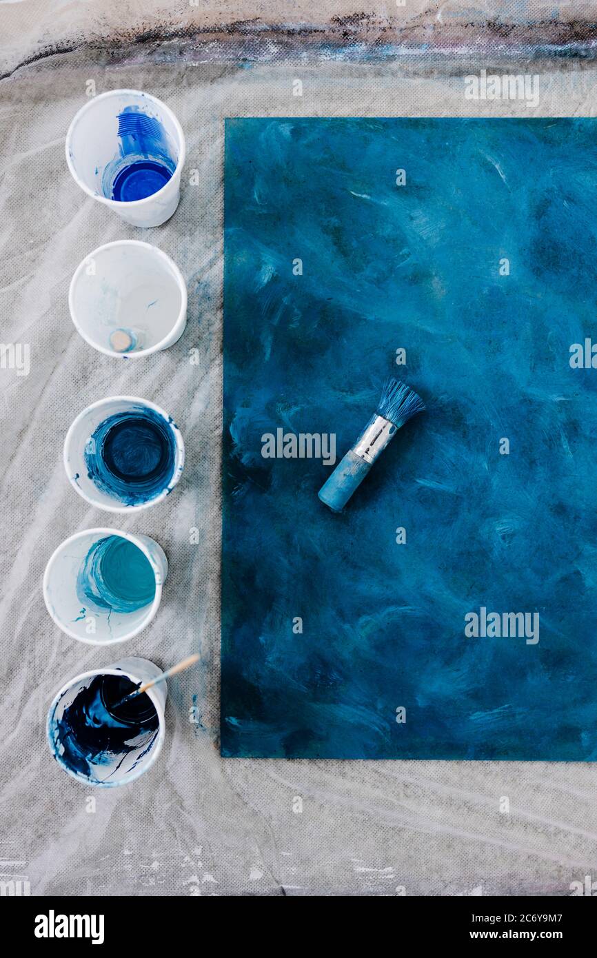arts and craft hobbies concept, blue and black acrylic painting with colors  in plastic cups and mixed painting tools next to it while the work is in p  Stock Photo - Alamy