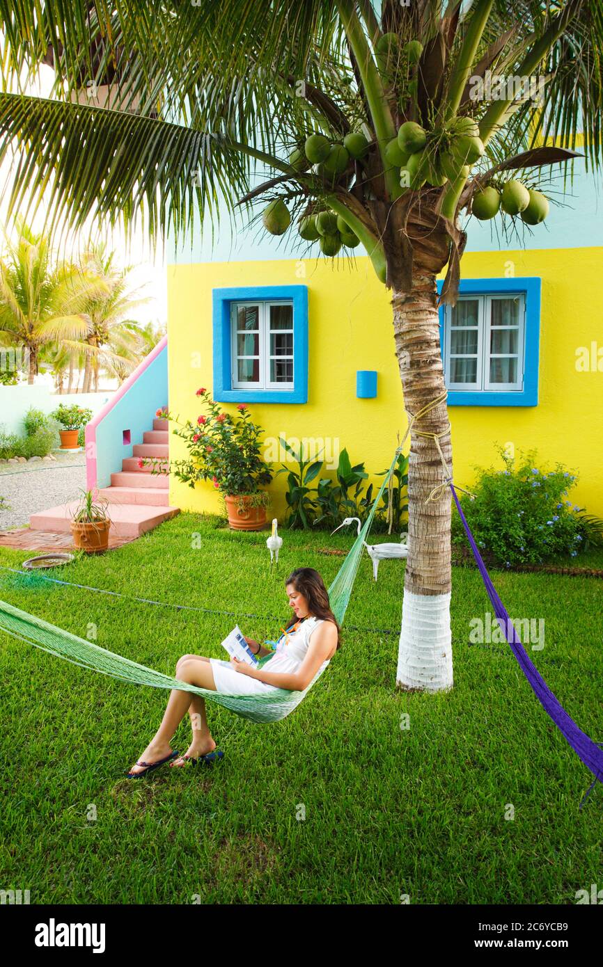 A young lady reads in a hammock outside a colorful bungalow in on the Pacific coast of Mexico. Stock Photo