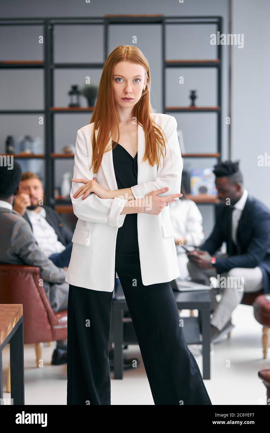 Beautiful serious woman in white blazer and with red hair, look at ...