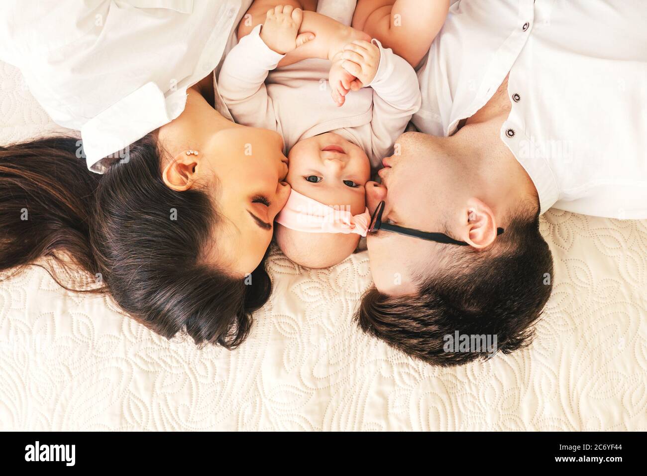 Happy young father, mother and cute baby boy lying on light bed ...