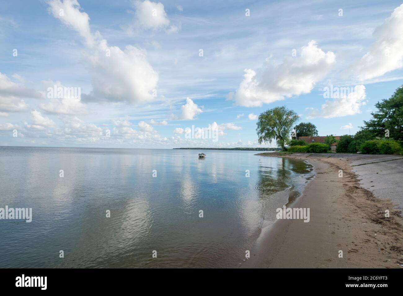 A solitary small boat is moored on the curvy beach shores of the Baltic Sea lagoon on a summer day. In NIda, Curonian Spit, Lithuania. Stock Photo