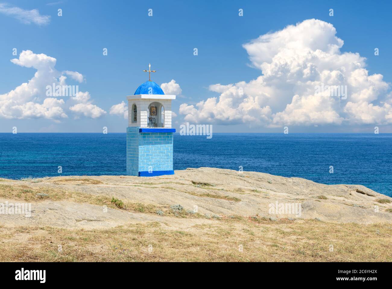 Traditional Greek small church or chapel. Blue sky with white clouds and sea in background Stock Photo