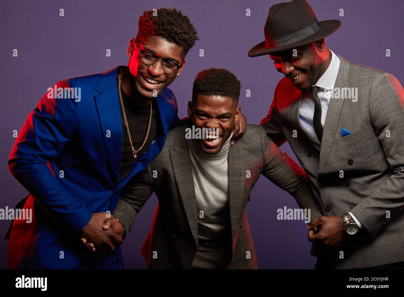 Studio shot of group of African male young adult friends wearing smart suits having fun and laughing over dark violet background Stock Photo