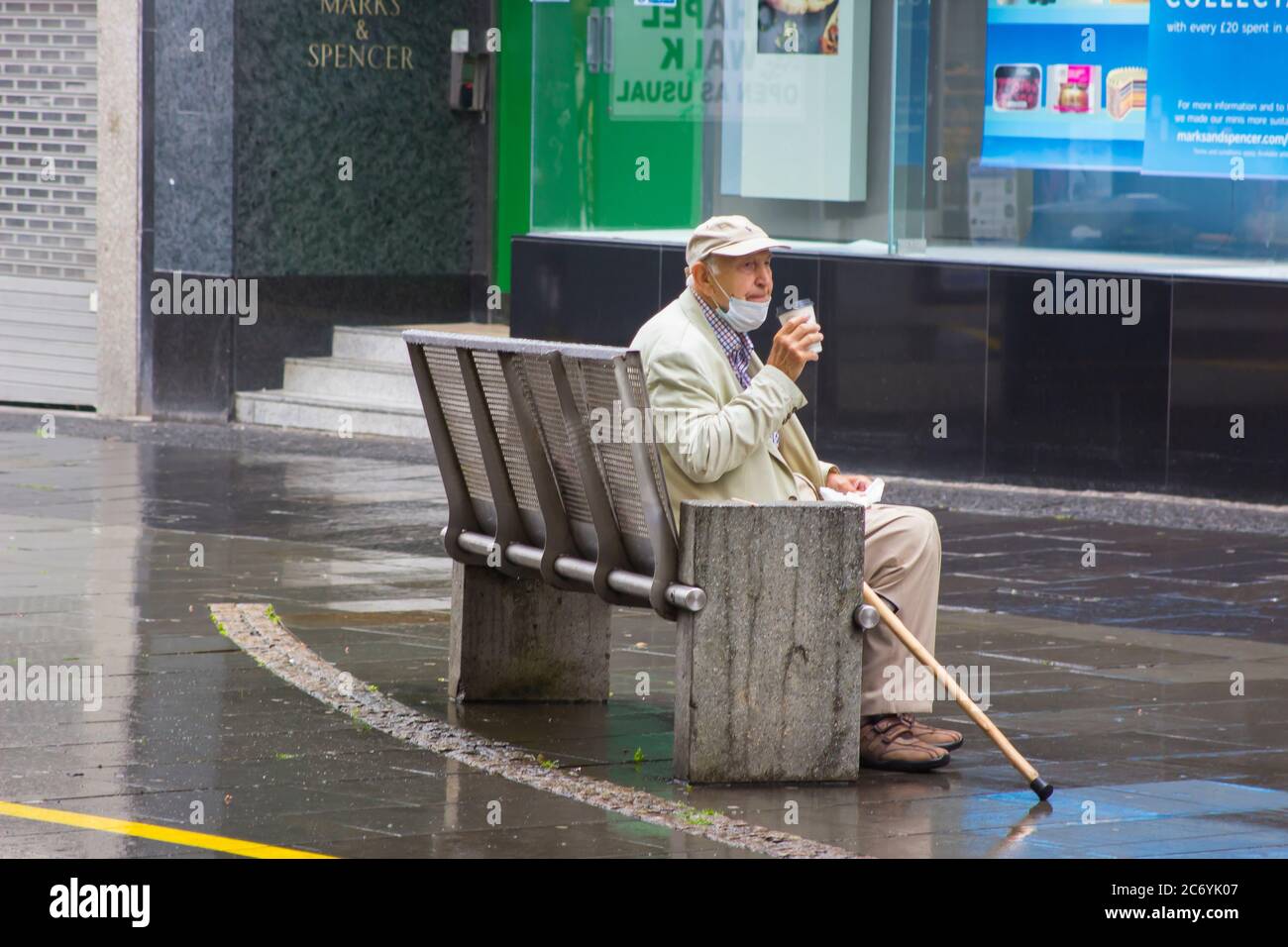 8 July 2020 An elderly gentleman with a face mask relaxes with a cup of hot coffe outside the Marks and Spencer store on Fargate in Sheffield City Cen Stock Photo