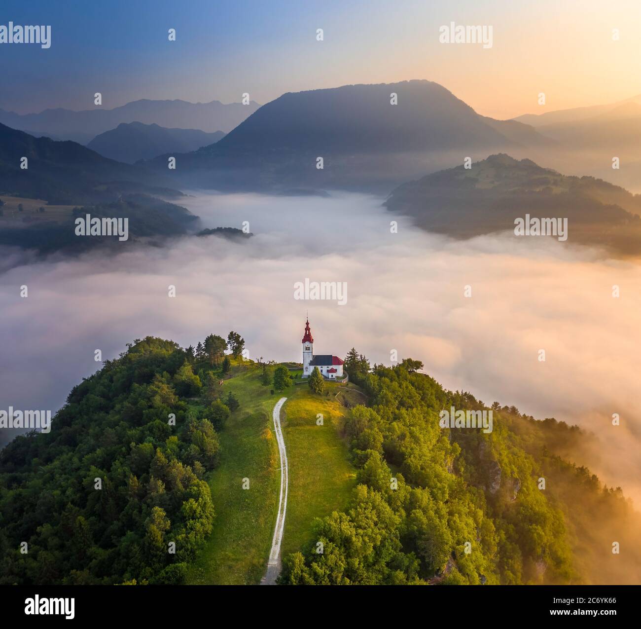 Šebrelje, Slovenia - Aerial drone view of the beautiful hilltop church of St.Ivan (Sv. Ivan Cerkev) at sunrise with huge morning fog bellow and Julian Stock Photo