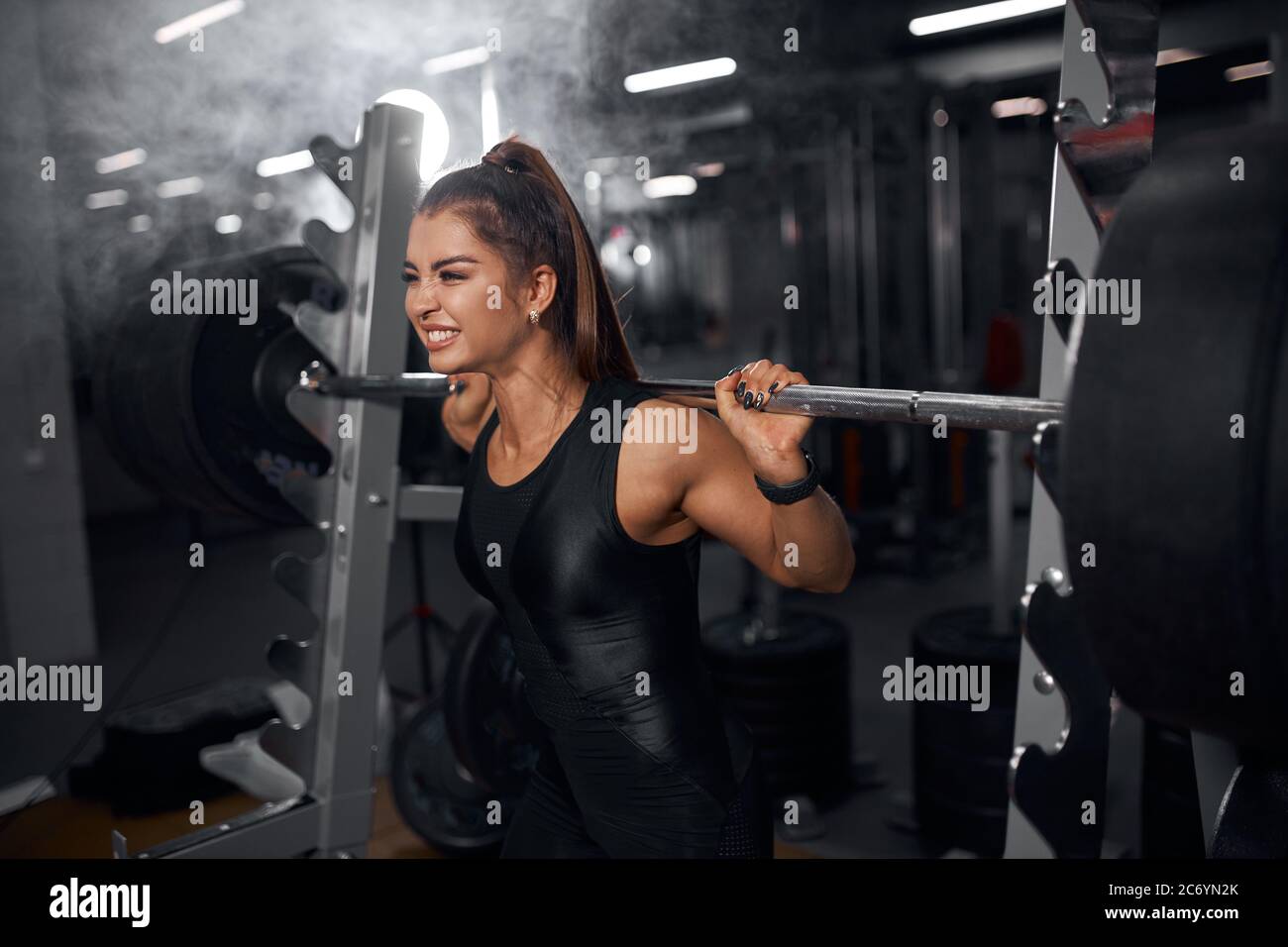 Young pretty female powerlifter trying to lift heavy weight, standing