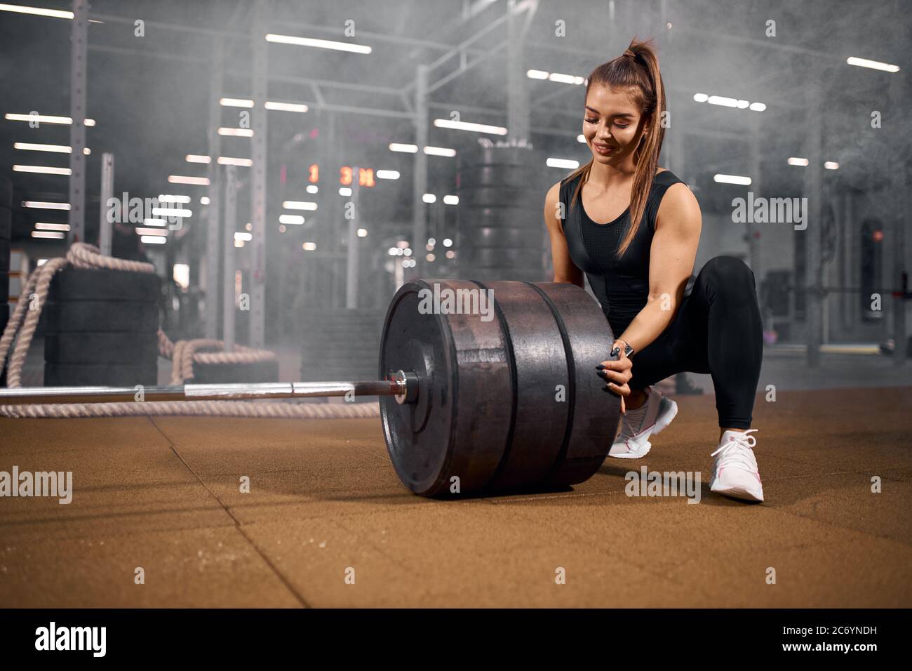 Charming joyful female powerlifter squatting in front of heavy barbell