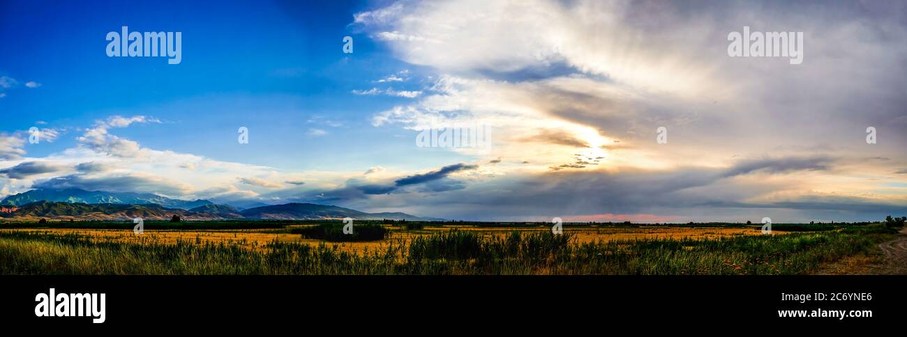 Panorama of a mountain valley in the summer, cloudy sky. Fairytale sunset over the mountain peaks, amazing nature, summer in the mountains. Travel. be Stock Photo