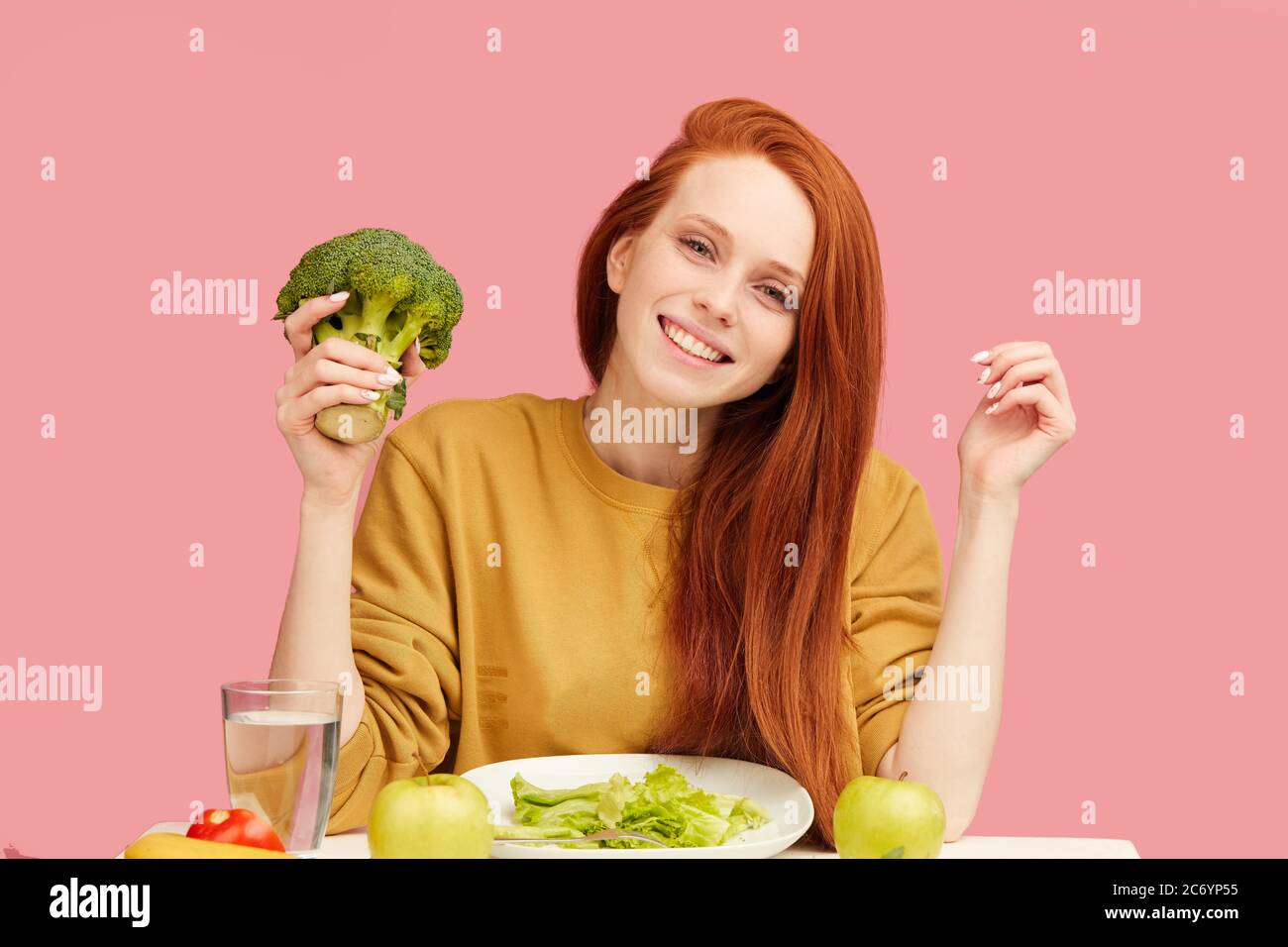 cheerful young lovely woman with long ginger hair dressed in yellow  sweatshirt with vegetarian food set with broccoli, against pink background.  Health Stock Photo - Alamy