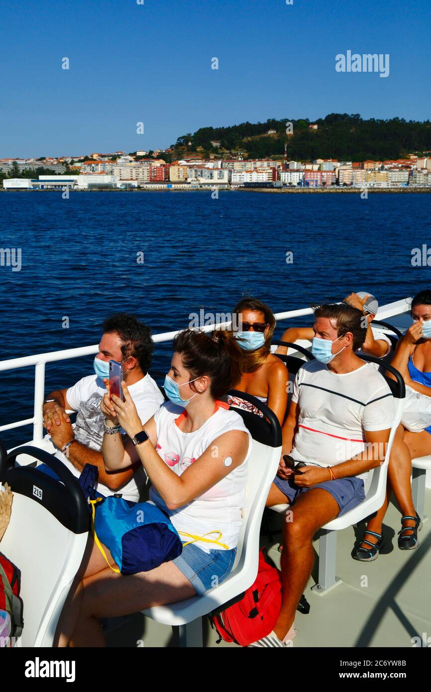 12th July 2020, Ria de Vigo, Galicia, northern Spain: Passengers wearing face masks on the ferry from Vigo to the Cies Islands, a popular tourist destination off the coast of Galicia. Spain has relaxed travel restrictions from 21st June after a strict lockdown to control the Covid 19 coronavirus and many Spaniards are returning to the beaches. Wearing face masks is still mandatory on public transport. In the background is the small town of Cangas. Stock Photo